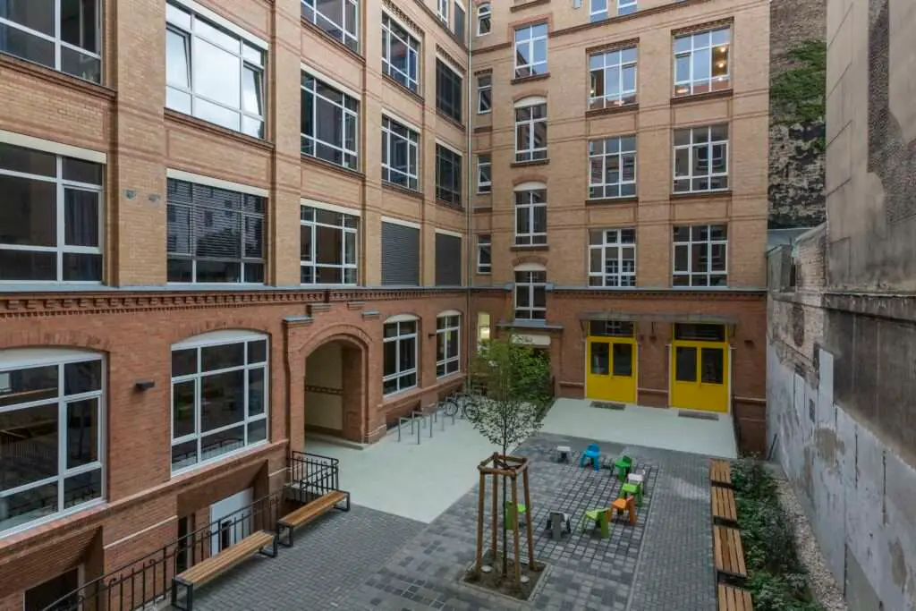 Innenhof mit bunten Stühlen, eine Baum und Backsteinfassade