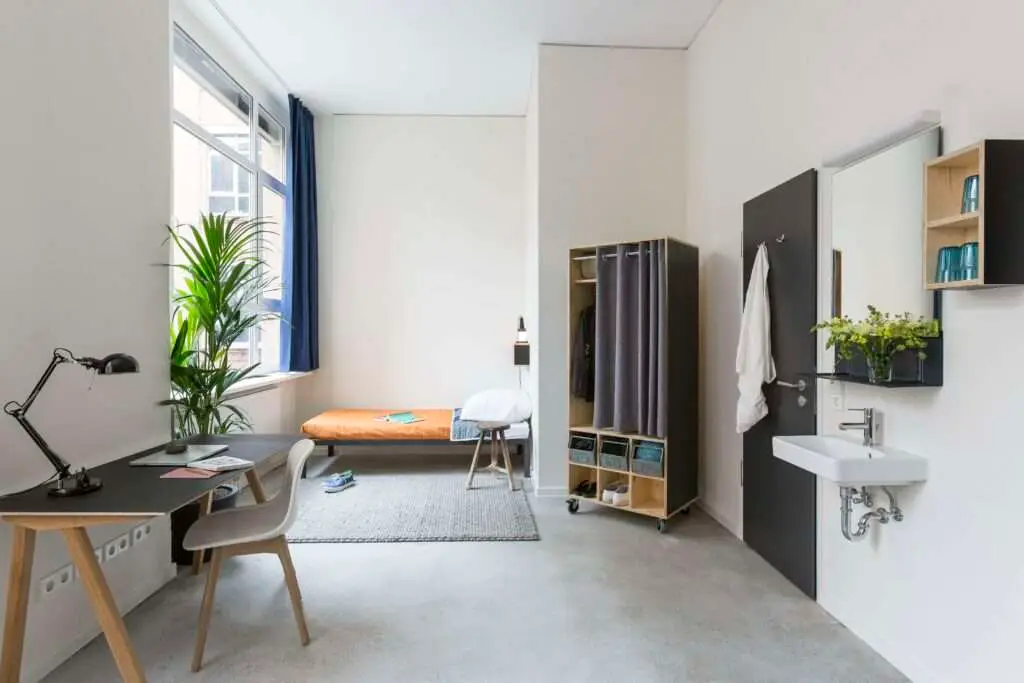 ein Zimmer Apartment mit Bett, Schreibtisch und Waschbereich