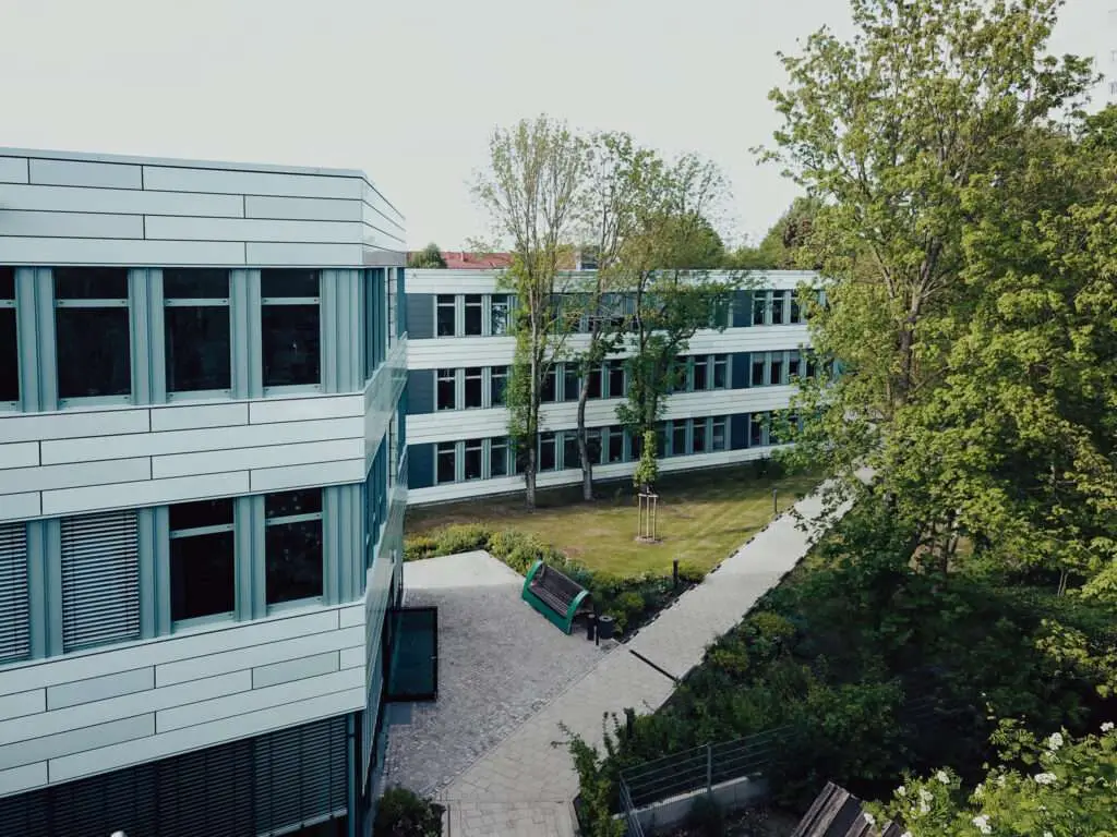 Außenansicht eines Bürogebäudes mit Bäumen, Wiesen und Bänken