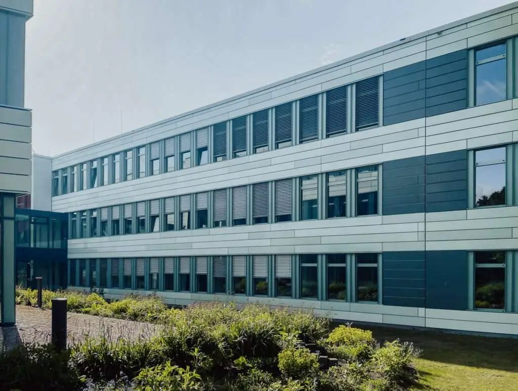 Fensterfront mit halb heruntergelassenem Sonnenschutz und Büschen